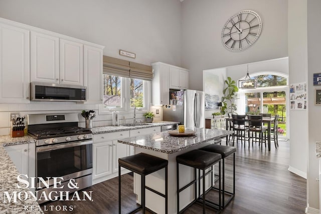 kitchen with appliances with stainless steel finishes, a sink, a towering ceiling, white cabinets, and plenty of natural light