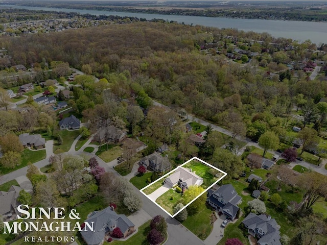 aerial overview of property's location with a large body of water, nearby suburban area, and a heavily wooded area