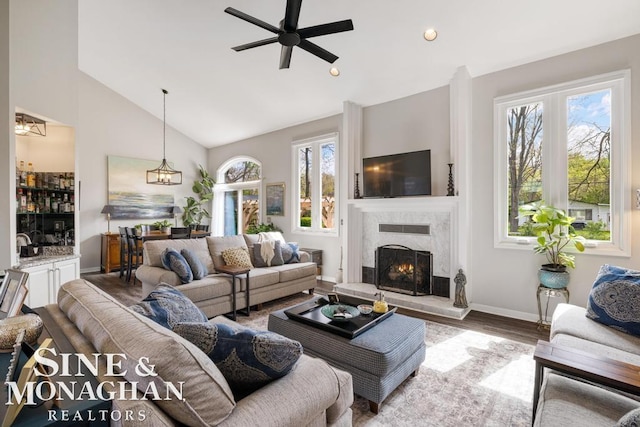 living area with wood finished floors, ceiling fan, a premium fireplace, baseboards, and high vaulted ceiling