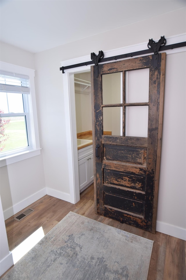 7272 S 7 Mile Rd, Freeland, MI 48623 - unfurnished bedroom with a barn door, light wood-style flooring, and baseboards