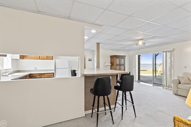 kitchen with a drop ceiling, freestanding refrigerator, light carpet, open floor plan, and a breakfast bar area