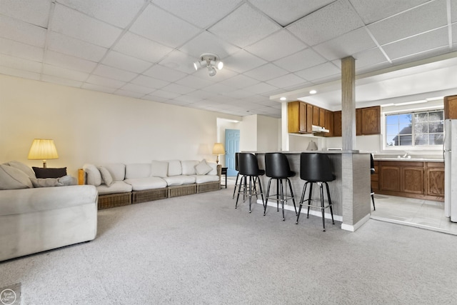living room featuring light colored carpet, bar with sink, and a paneled ceiling