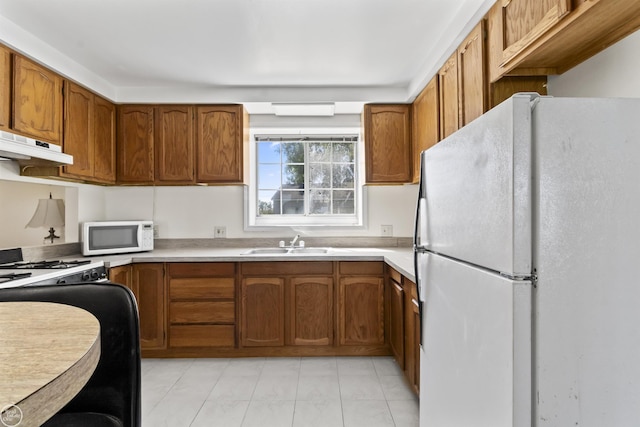 kitchen with white appliances, under cabinet range hood, a sink, and brown cabinets