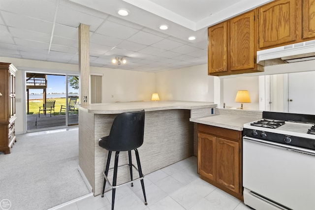 kitchen with gas range gas stove, light countertops, under cabinet range hood, a breakfast bar area, and recessed lighting