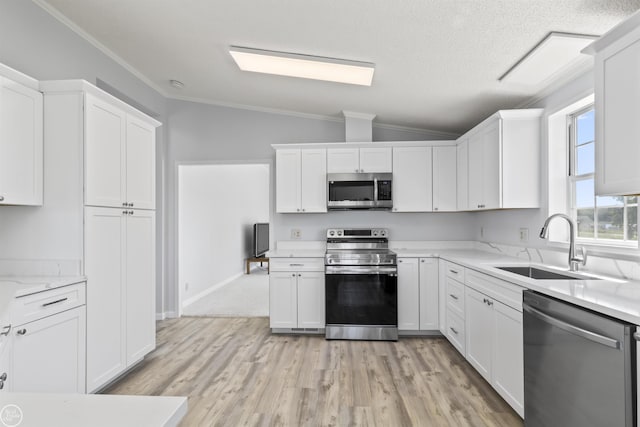 kitchen featuring stainless steel appliances, lofted ceiling, a sink, white cabinetry, and ornamental molding