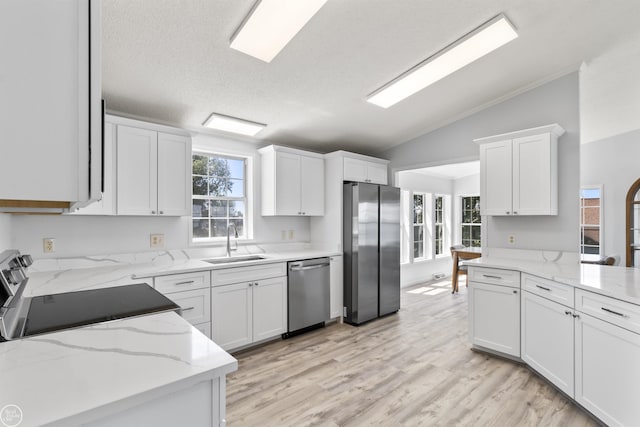 kitchen with stainless steel appliances, vaulted ceiling, a sink, white cabinets, and light stone counters