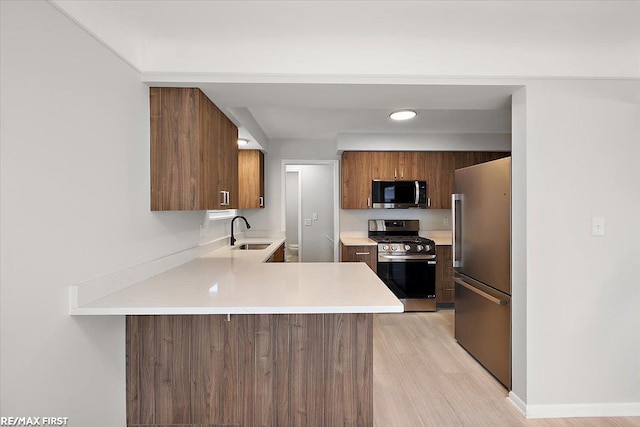 kitchen with appliances with stainless steel finishes, a sink, a peninsula, light countertops, and light wood-style flooring