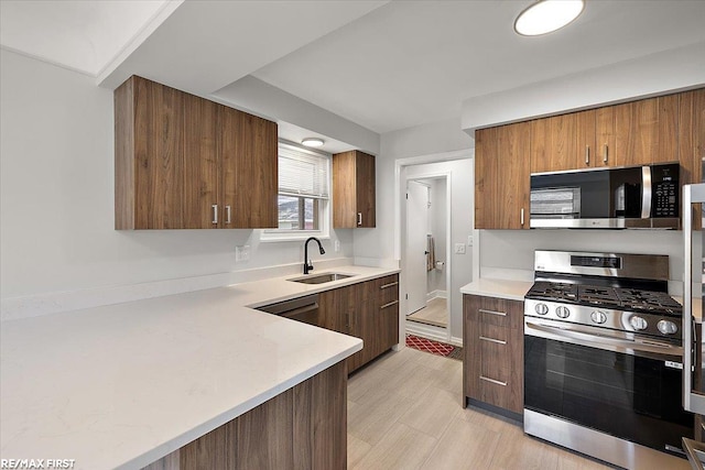 kitchen with appliances with stainless steel finishes, a sink, light countertops, and brown cabinetry