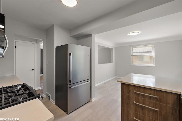 kitchen with high end refrigerator, light countertops, baseboards, light wood-style floors, and gas range