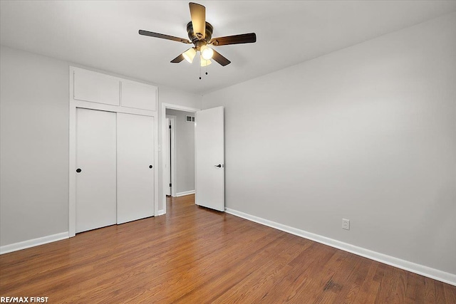 unfurnished bedroom with baseboards, wood finished floors, a closet, and a ceiling fan