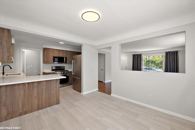 kitchen featuring appliances with stainless steel finishes, a sink, light countertops, baseboards, and a peninsula