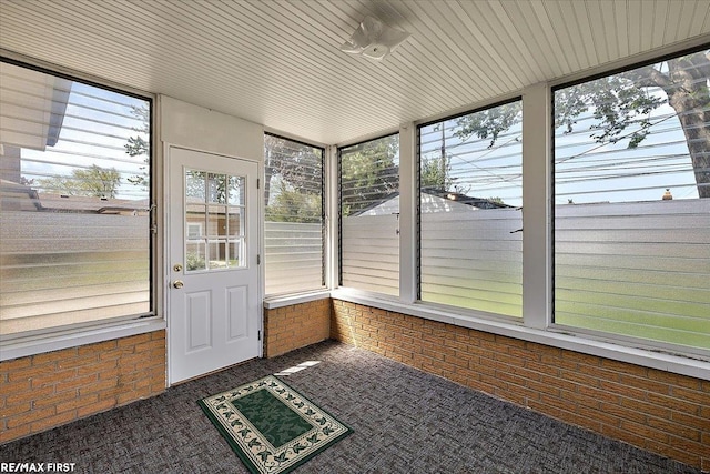 unfurnished sunroom featuring plenty of natural light, brick wall, and carpet