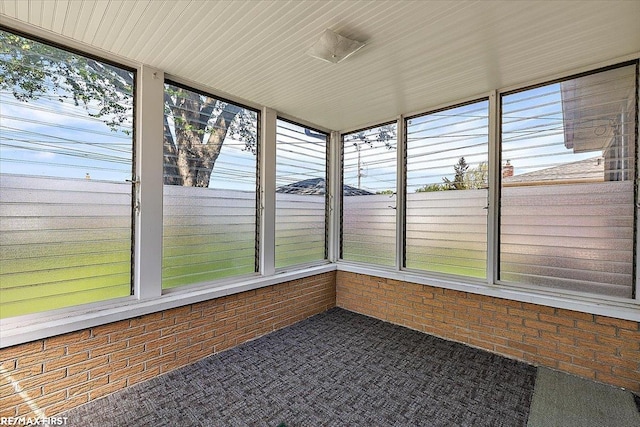 unfurnished sunroom featuring brick wall, carpet flooring, and plenty of natural light