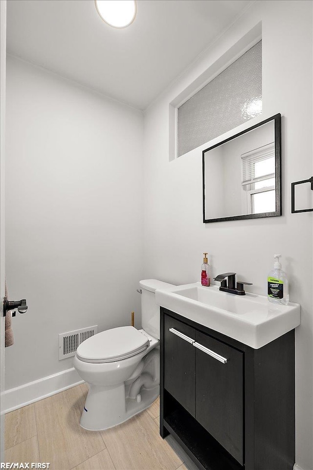 half bathroom with toilet, wood finished floors, and vanity