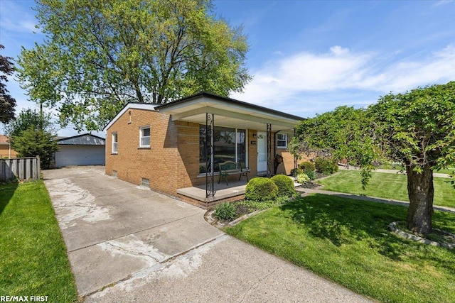view of front of home with covered porch, a front lawn, brick siding, an outbuilding, and a garage