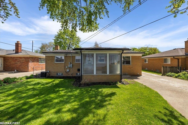 rear view of house with brick siding, a yard, a chimney, and central AC