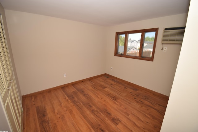 unfurnished bedroom with wood finished floors, an AC wall unit, and baseboards