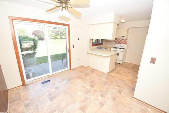 kitchen with white range with gas stovetop, light countertops, a peninsula, under cabinet range hood, and decorative backsplash