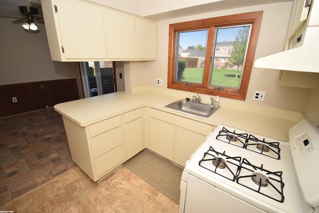 kitchen with a sink, white gas range, a peninsula, light countertops, and a ceiling fan
