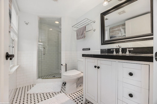 full bath featuring a stall shower, tile walls, toilet, tile patterned flooring, and wainscoting