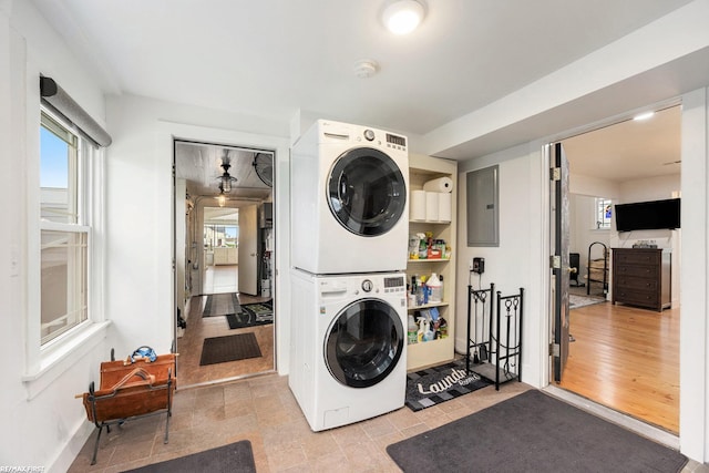 laundry area featuring stacked washing machine and dryer, electric panel, and baseboards