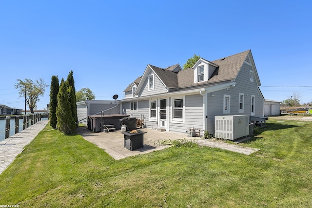 rear view of property with a patio, a hot tub, a lawn, roof with shingles, and an outdoor fire pit