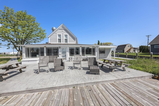 rear view of house with a sunroom, a wooden deck, and a patio area