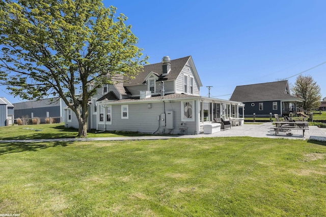 rear view of house with a patio, a yard, a shingled roof, and a sunroom