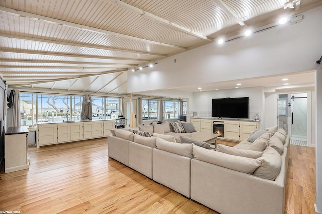 living area featuring beam ceiling, a glass covered fireplace, light wood-style flooring, and high vaulted ceiling