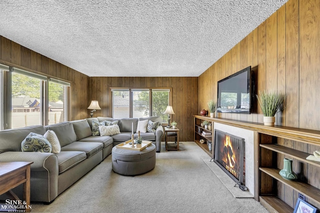 carpeted living room featuring wood walls, healthy amount of natural light, a fireplace with flush hearth, and a textured ceiling