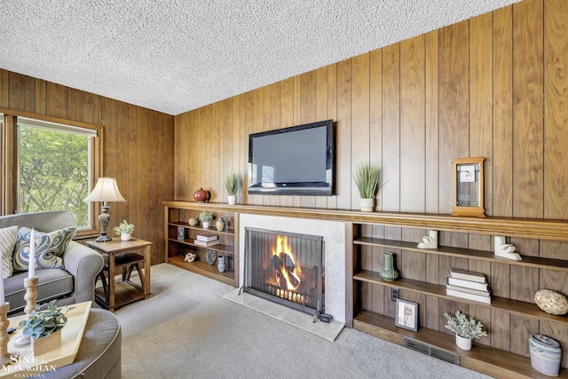 living area with a lit fireplace, a textured ceiling, wooden walls, and carpet flooring