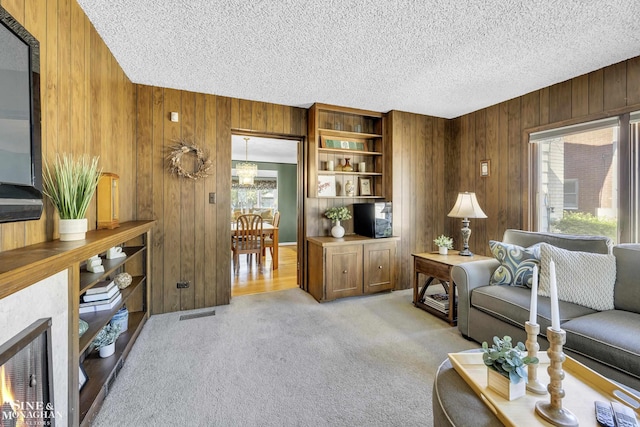 living room featuring wooden walls, plenty of natural light, a textured ceiling, and light carpet