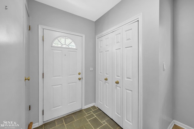 foyer featuring baseboards and dark stone finish flooring