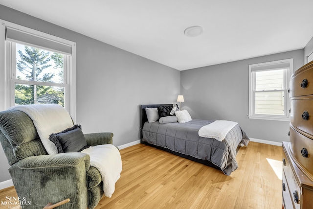 bedroom with multiple windows, light wood-style floors, and baseboards