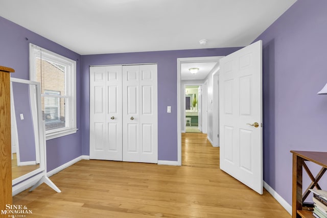 unfurnished bedroom featuring light wood finished floors, baseboards, and a closet