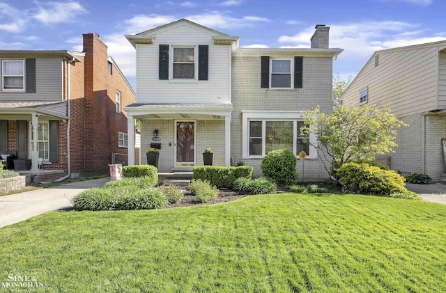 traditional-style home featuring a front yard, a chimney, brick siding, and covered porch