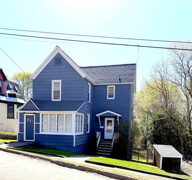 traditional home featuring roof with shingles, a storage unit, an outdoor structure, and fence