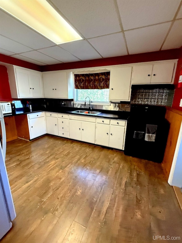 kitchen featuring a sink, a paneled ceiling, light wood-type flooring, white cabinets, and decorative backsplash