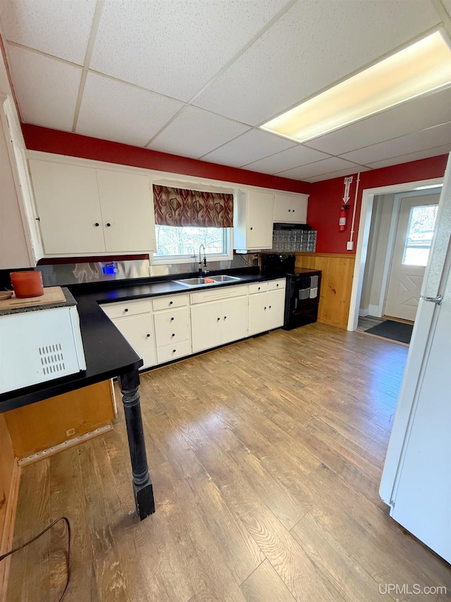 kitchen with a sink, white appliances, a drop ceiling, white cabinetry, and dark countertops