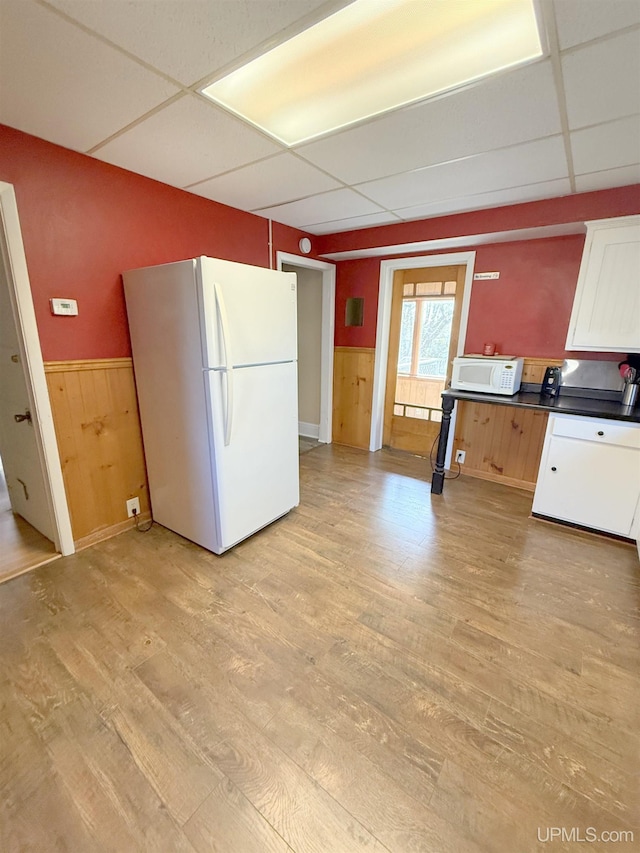 kitchen with white appliances, a paneled ceiling, wainscoting, light wood-style floors, and dark countertops