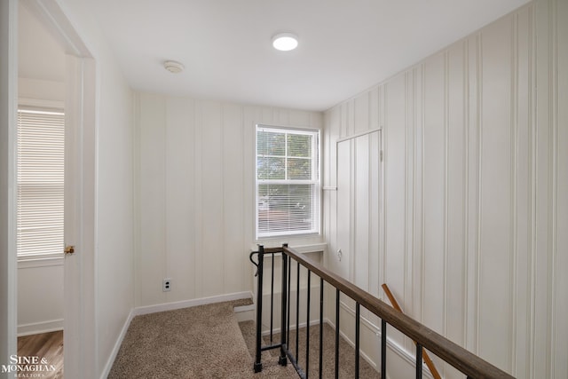 corridor with baseboards, an upstairs landing, and carpet flooring