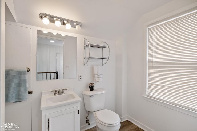 bathroom with toilet, vanity, lofted ceiling, baseboards, and wood finished floors