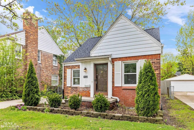 bungalow with brick siding, a shingled roof, an outbuilding, and a detached garage