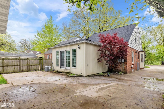 rear view of house featuring fence, roof with shingles, central AC unit, a patio area, and brick siding