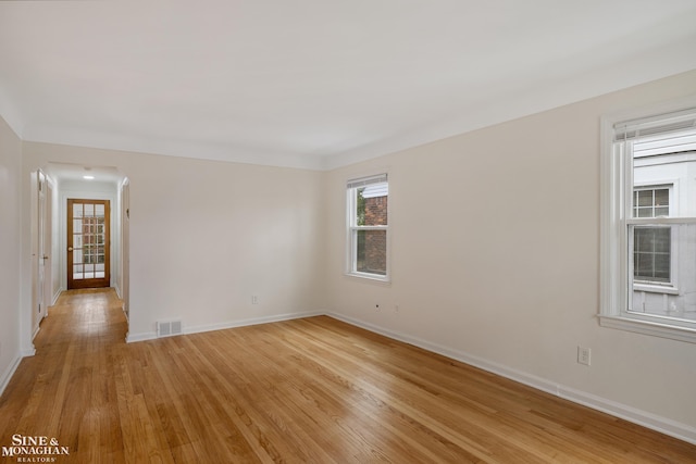 spare room featuring light wood-style floors, baseboards, and arched walkways