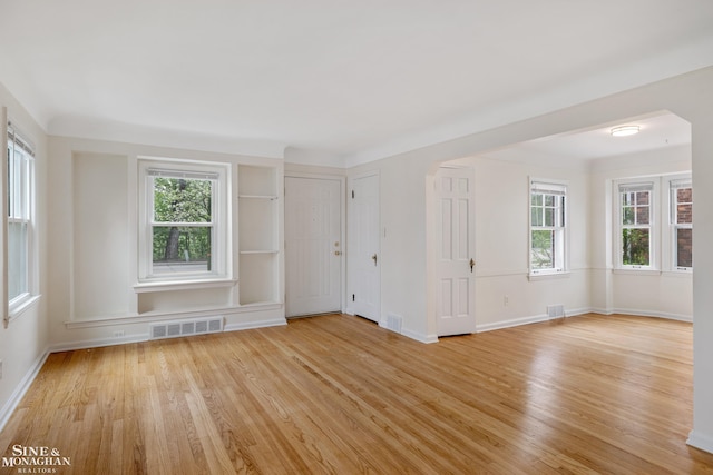 unfurnished room featuring light wood-style floors, healthy amount of natural light, baseboards, and arched walkways