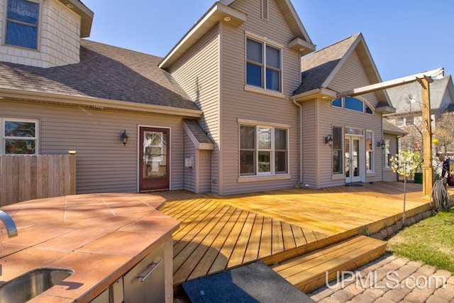 212 S 1st Ave, Escanaba, MI 49829 - rear view of property featuring a shingled roof, a wooden deck, a sink, and fence