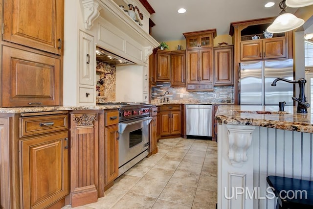 212 S 1st Ave, Escanaba, MI 49829 - kitchen featuring high end appliances, brown cabinets, backsplash, light stone countertops, and light tile patterned floors