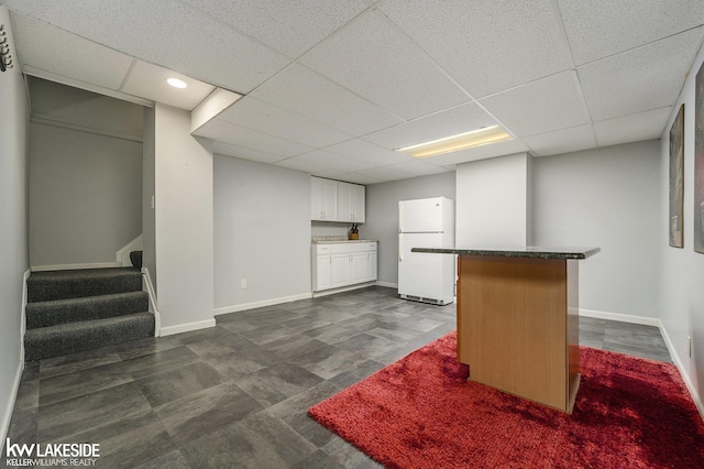 finished below grade area featuring freestanding refrigerator, a drop ceiling, a bar, baseboards, and stairs