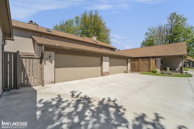 view of front of house featuring brick siding, a chimney, concrete driveway, and a gate